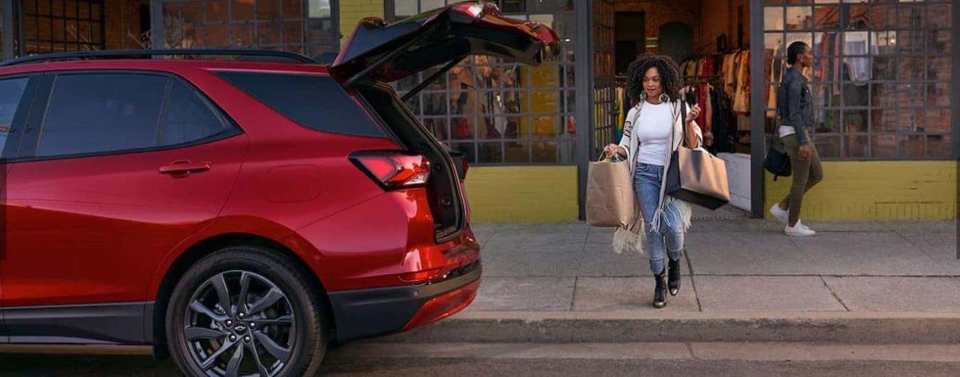 Woman carrying bags to the open hatchback of a red 2024 Chevy Equinox RS after searching for "Chevy dealer near me."