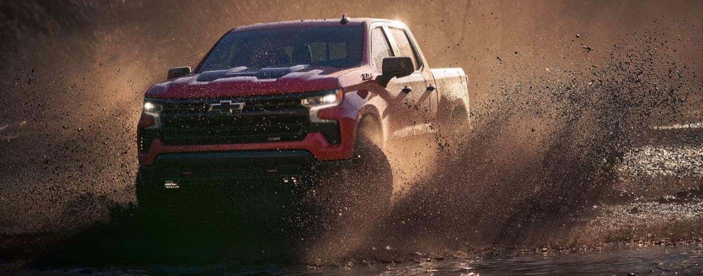 A red 2023 Chevy Silverado 1500 Z71 Trail Boss driving over a pool of mud.