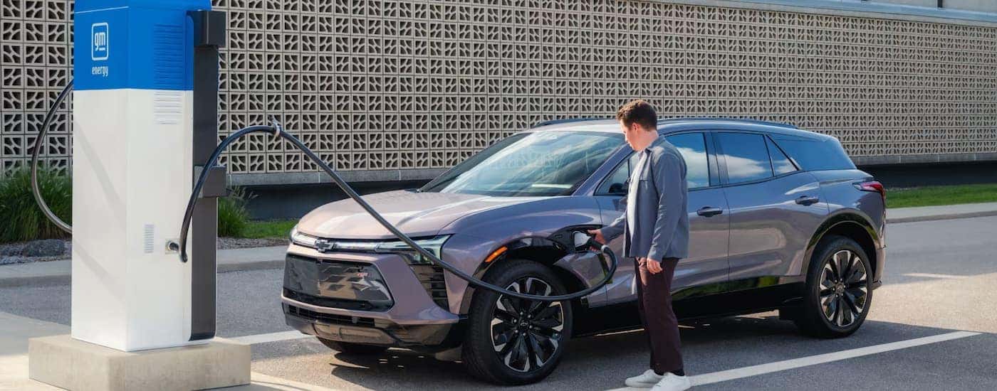 A man charging a grey 2024 Chevy Blazer EV parked at a charging station.
