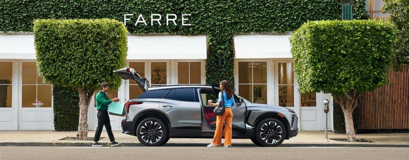 A silver 2024 Chevy Blazer EV is parked in front of a shop.