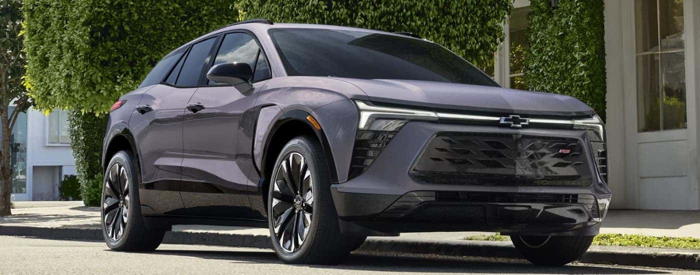A grey 2024 Chevy Blazer EV is parked near bushes.