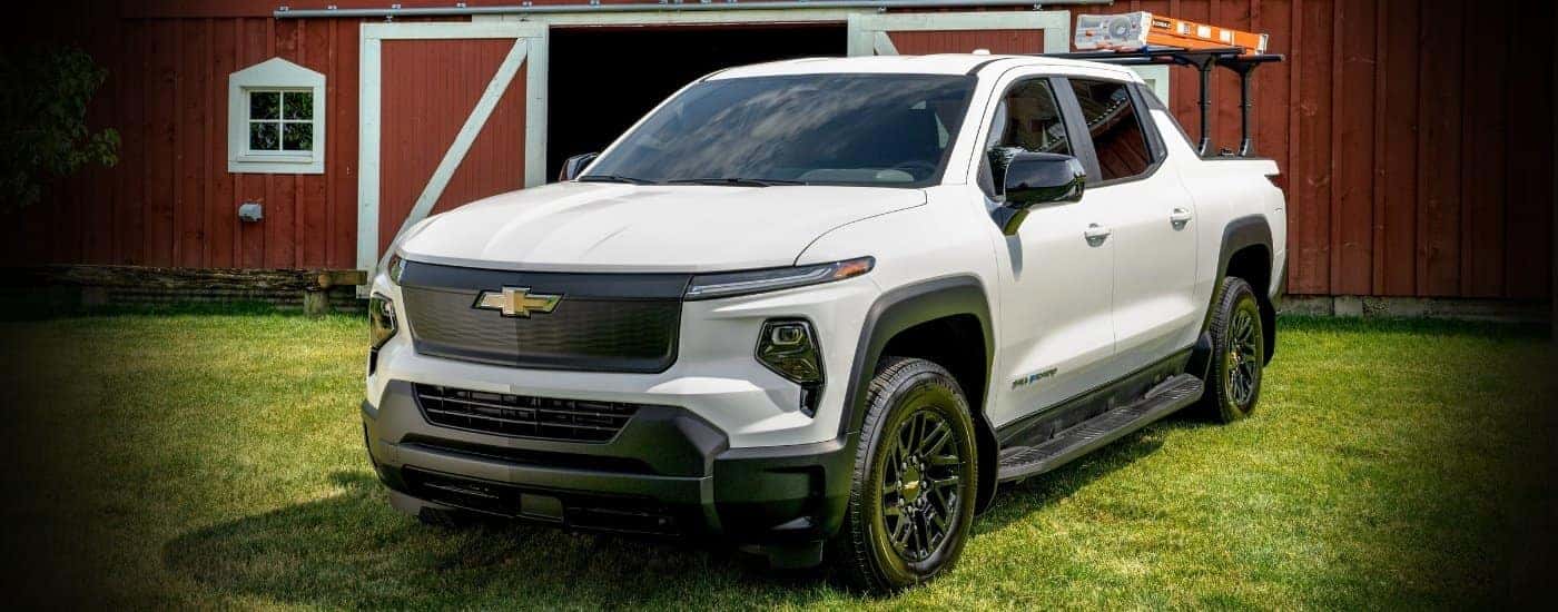 A white 2024 Chevy Silverado EV WT parked in front of a red barn.