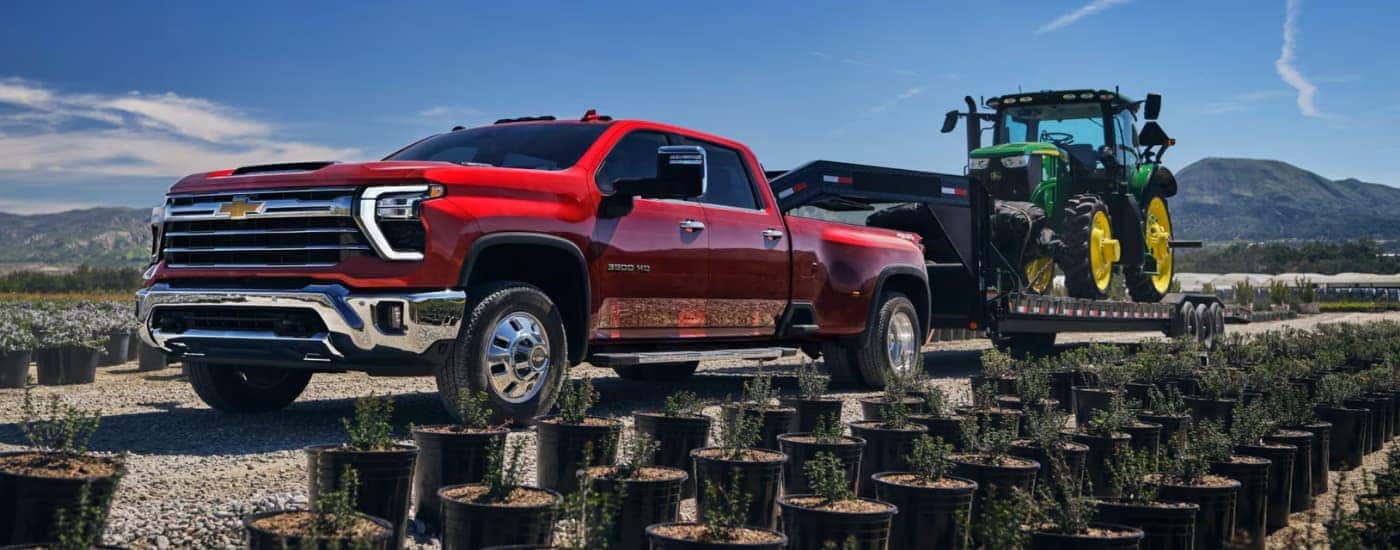 A red 2025 Chevy Silverado 3500 towing a tractor