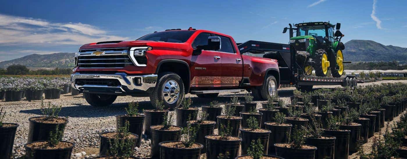 A red 2025 Chevy Silverado 3500 towing a tractor