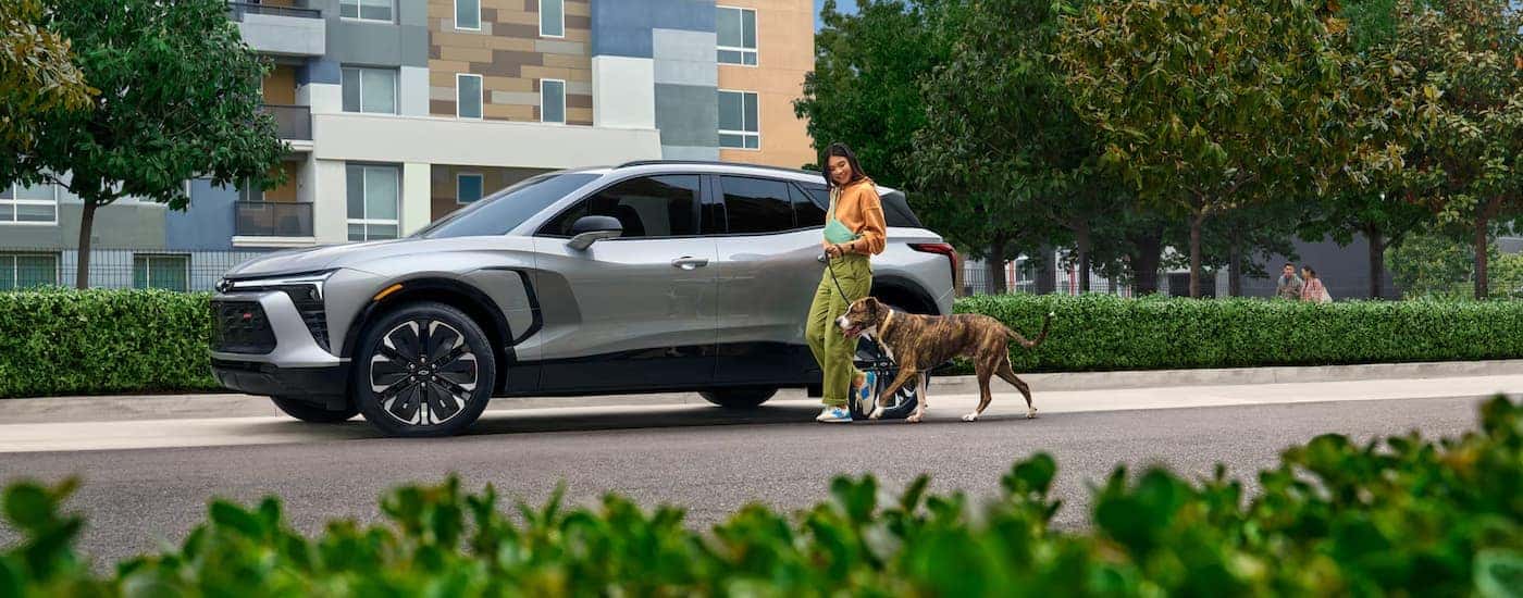 A woman walking by a white 2025 Chevy Blazer EV parked by a curb.