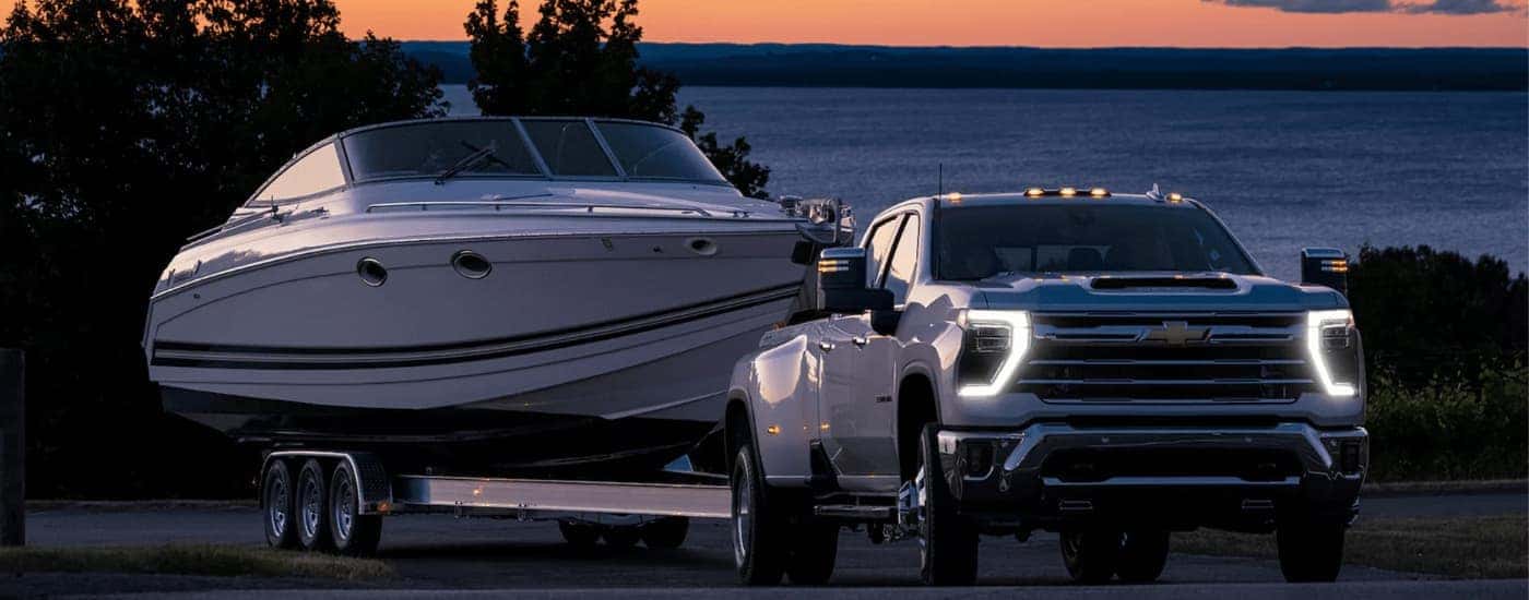 A white 2025 Chevy Silverado 3500 for sale is shown from the front while towing a boat.