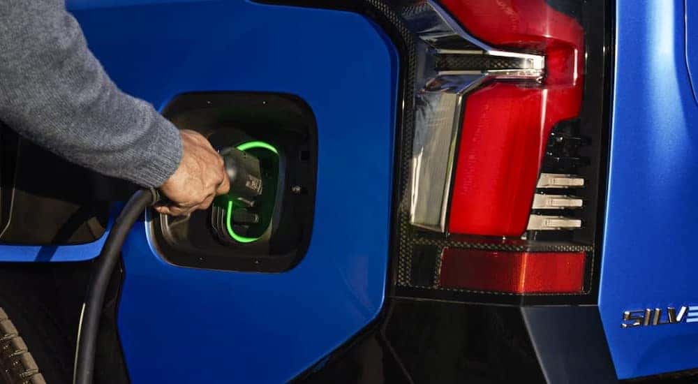 A person charging a blue 2025 Chevy Silverado EV.