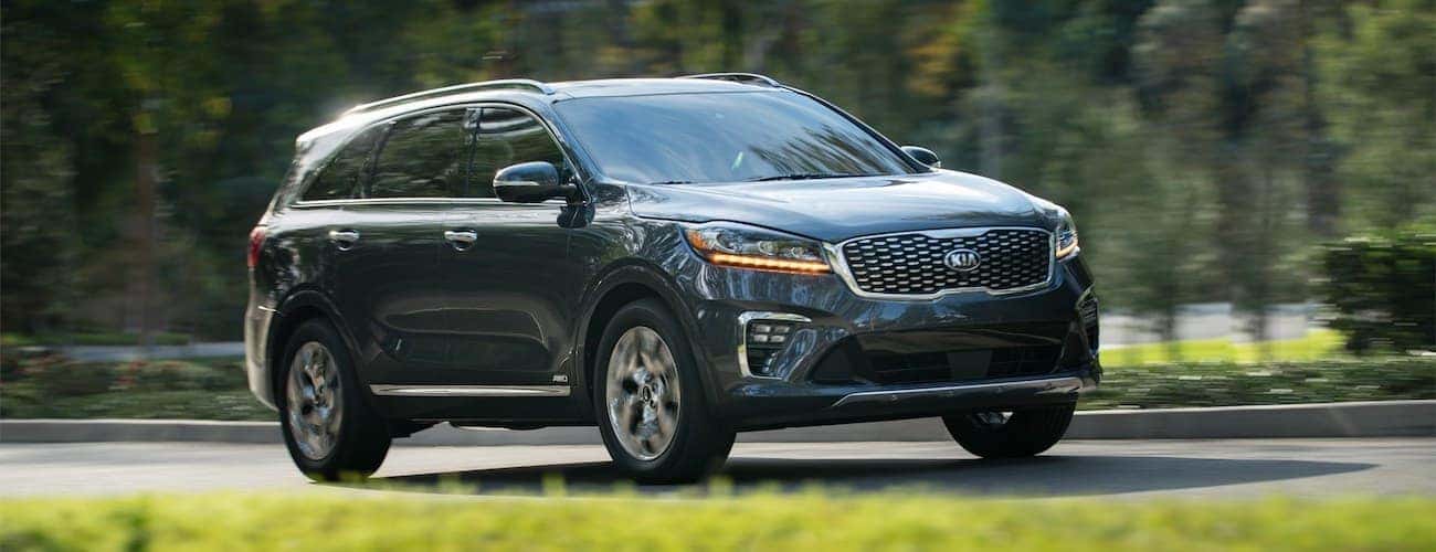 A dark grey 2020 Kia Sorento is driving on a tree-lined road.