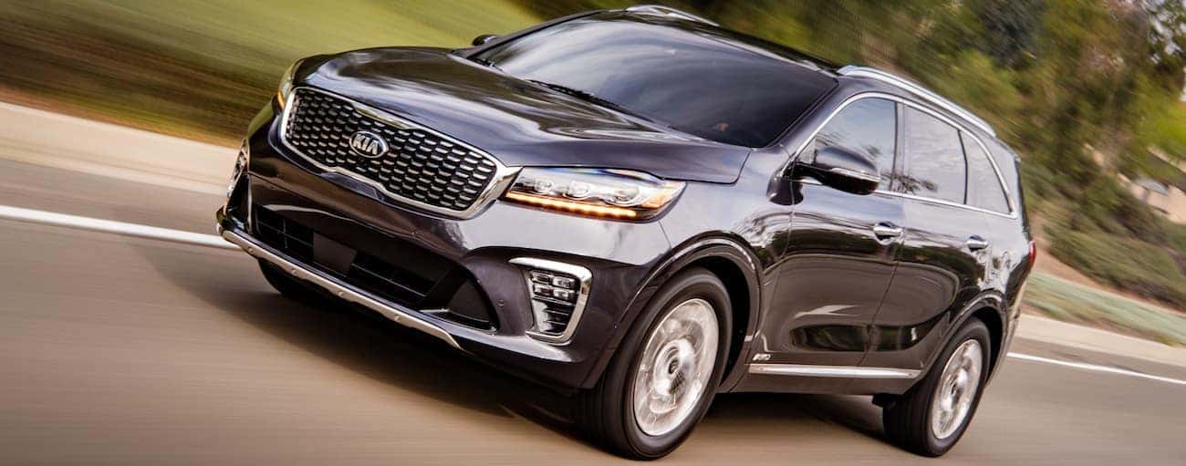 A dark grey 2020 Kia Sorento is driving on a road passing a lawn in Freehold, NJ.