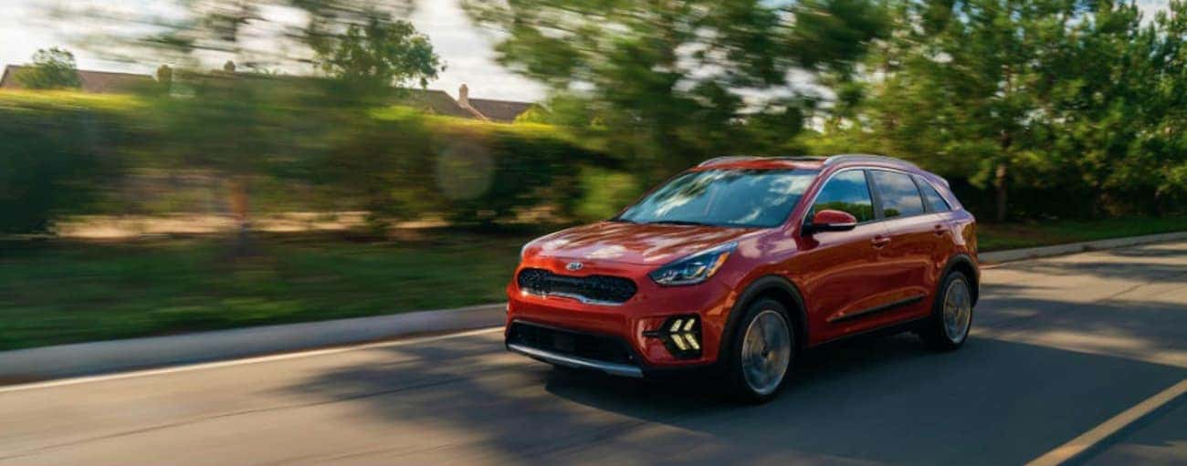 A red 2020 Kia Niro is driving on a tree-lined street near Freehold, NJ.