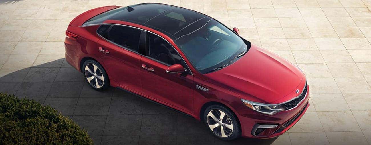 A red 2020 Kia Optima is parked on tan pavers after winning the 2020 Kia Optima vs 2020 Ford Fusion comparison.