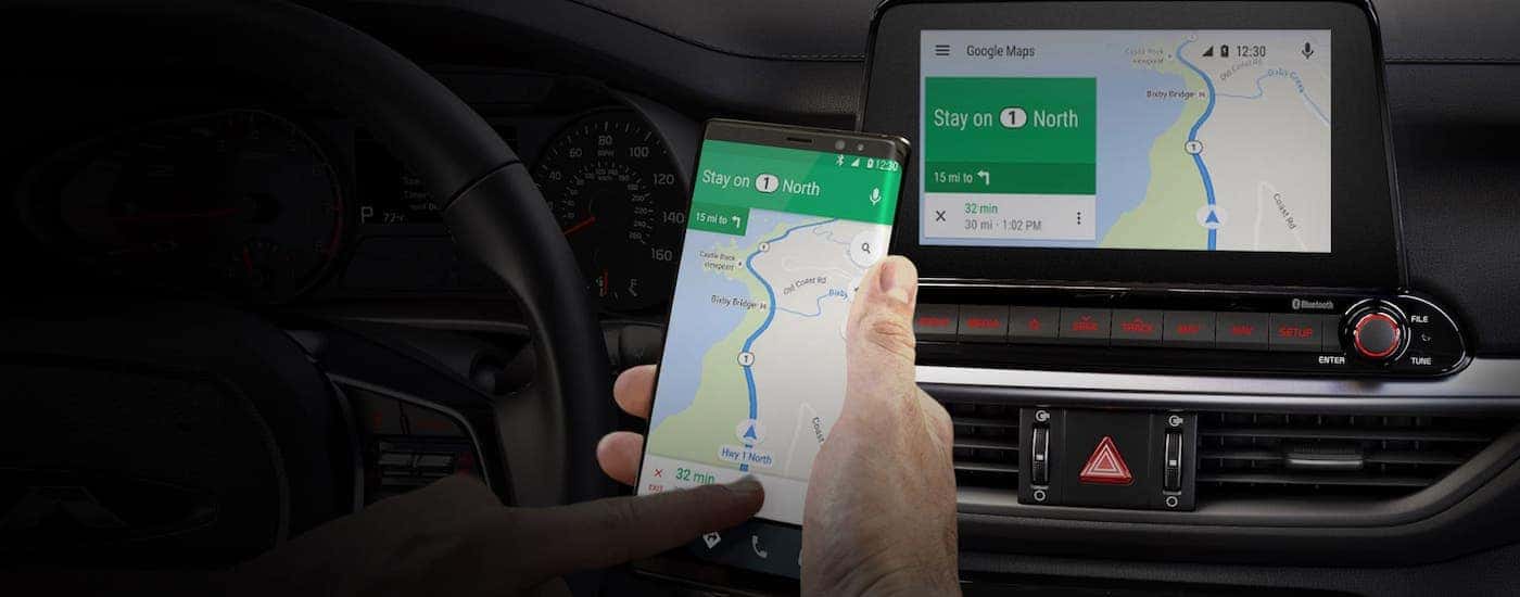 A driver is using his phone to get directions that appear on the touchscreen inside a 2020 Kia Forte.
