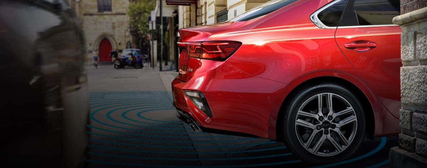 A red 202 Kia Forte is backing onto a Freehold, NJ, road with simulated safety lines around the rear end.