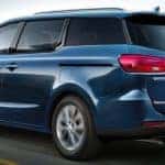 A blue 2021 Kia Sedona is driving on a coastal highway.