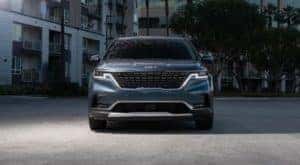 A blue 2022 Kia Carnival is shown from the front in front of a hotel.