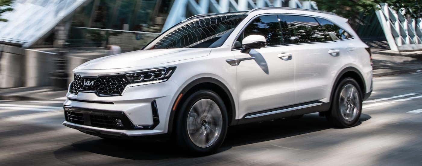 A white 2022 Kia Sorento Plug-In Hybrid is shown driving past a modern structure.