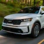 A white 2022 Kia Sorento Plug-In Hybrid is shown on a wooded road after visiting a Kia Sorento dealership.