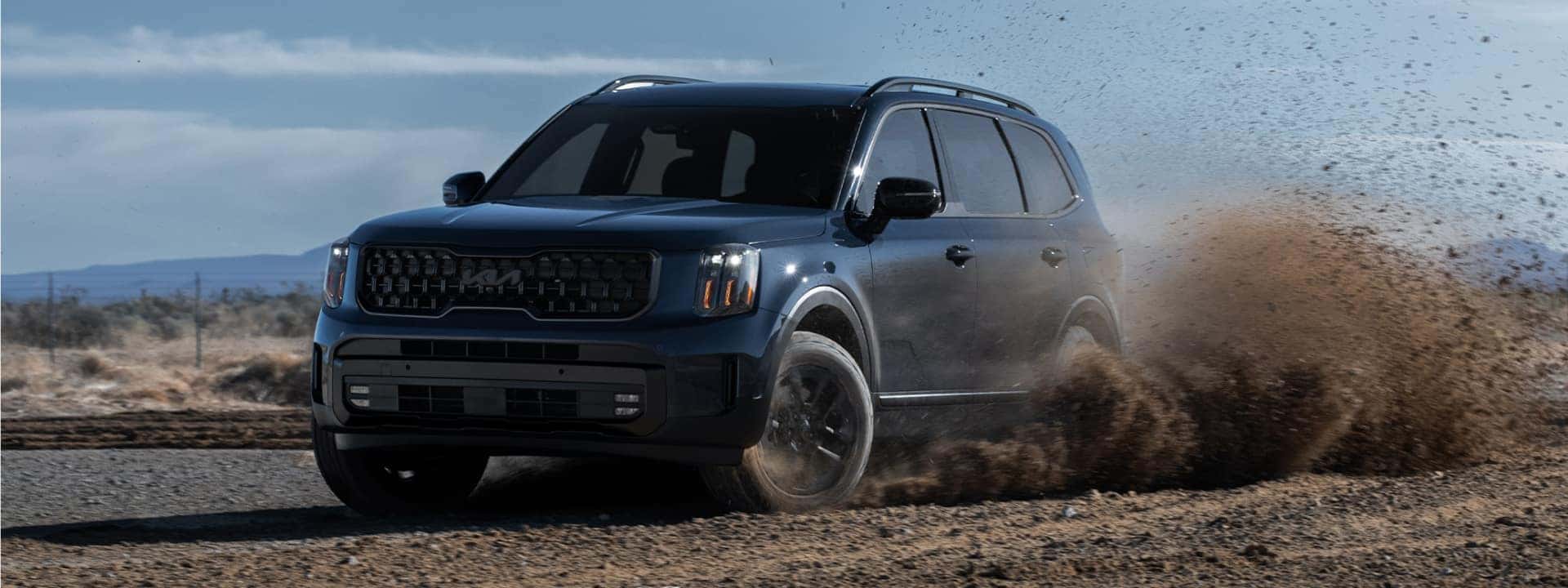 Kia SUV driving on dirt road, kicking up dirt in the air