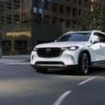 white 2025 mazda cx-90 driving down a highway