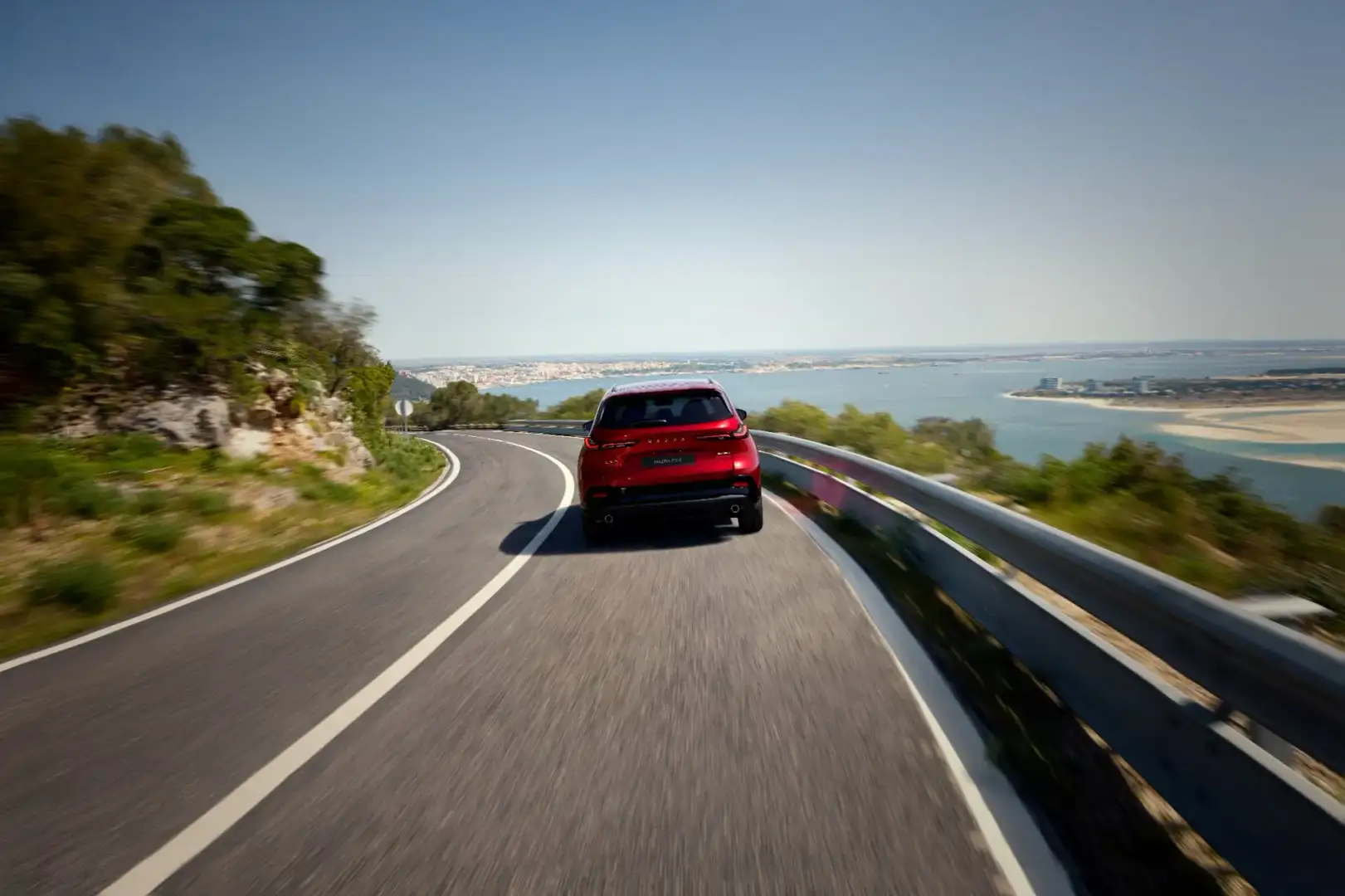 2026 Mazda CX-5 rear view driving along a scenic coastal highway