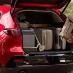Cargo area of a 2026 Mazda CX-5 loaded with two large checked bags and two carry-on suitcases behind the upright rear seats at Sport Mazda South in Orlando, Florida