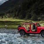 Jeep Wrangler with top off driving through river in front of a mountain