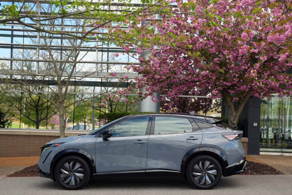 New Nissan Ariya parked in front of glass building and cherry blossom tree