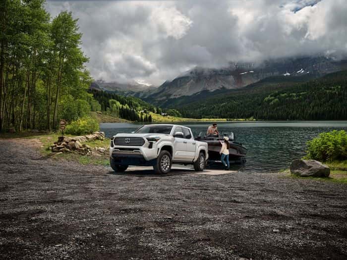 White Toyota Tacoma Limited with a boat trailer beside a mountain lake