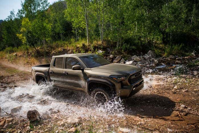 Toyota Tacoma driving through a wooded rocky creek