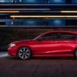 A red Honda Civic in profile, parked next to a building at night.