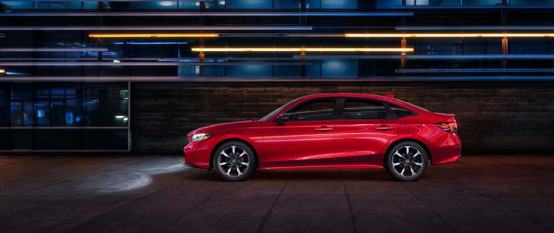 A red Honda Civic in profile, parked next to a building at night.
