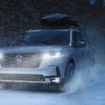 A silver Honda Pilot driving through the snow at night.