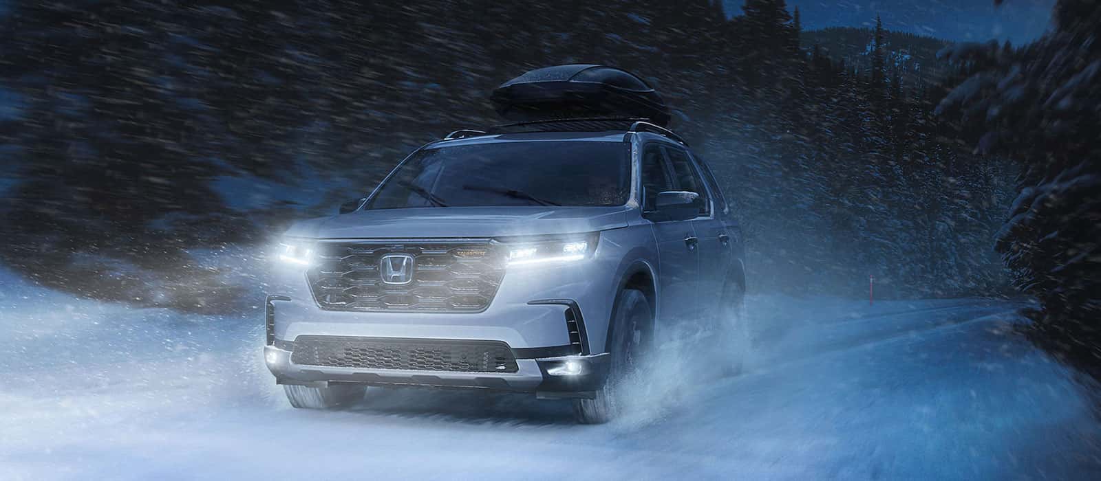 A silver Honda Pilot driving through the snow at night.