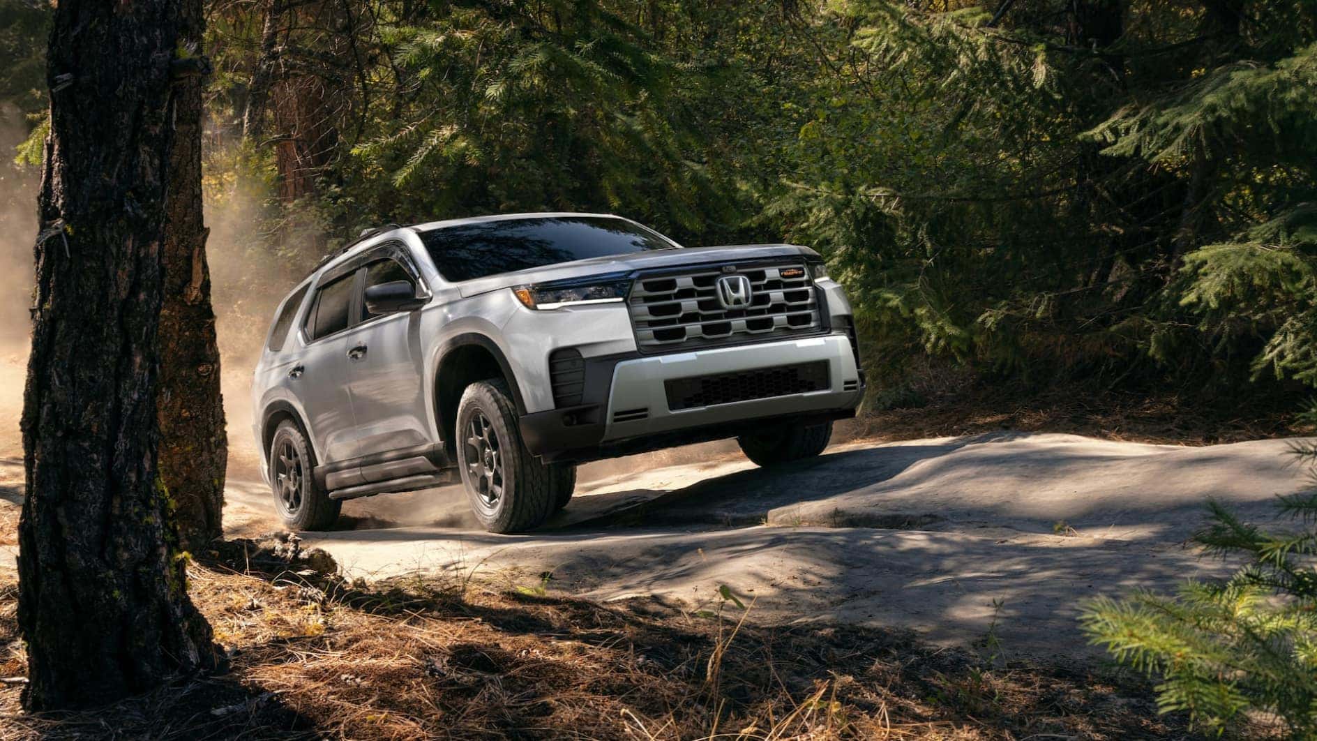 A white Honda Pilot driving on a bumpy road through a forest.LT