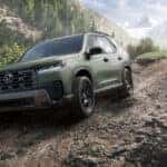 green Honda Pilot driving down a muddy hill in a mountain range.