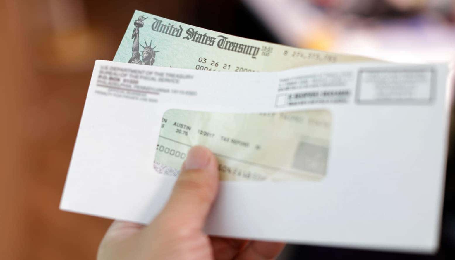 A person holding their tax refund check while it slides out of an envelope