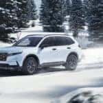 A white Honda CR-V Hybrid driving on a snowy road.