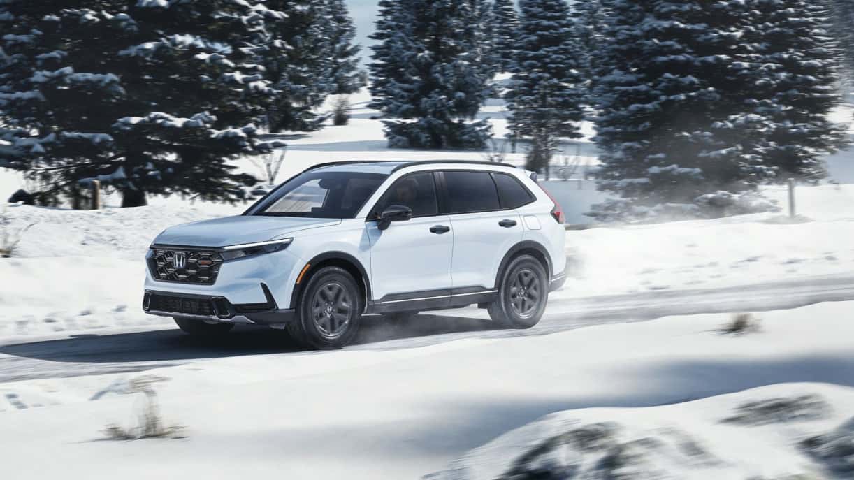 A white Honda CR-V Hybrid driving on a snowy road.