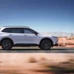 A silver Honda CR-V Driving down a road in profile through a desert.