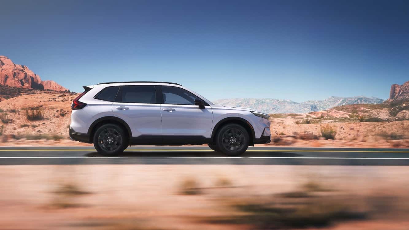 A silver Honda CR-V Driving down a road in profile through a desert.