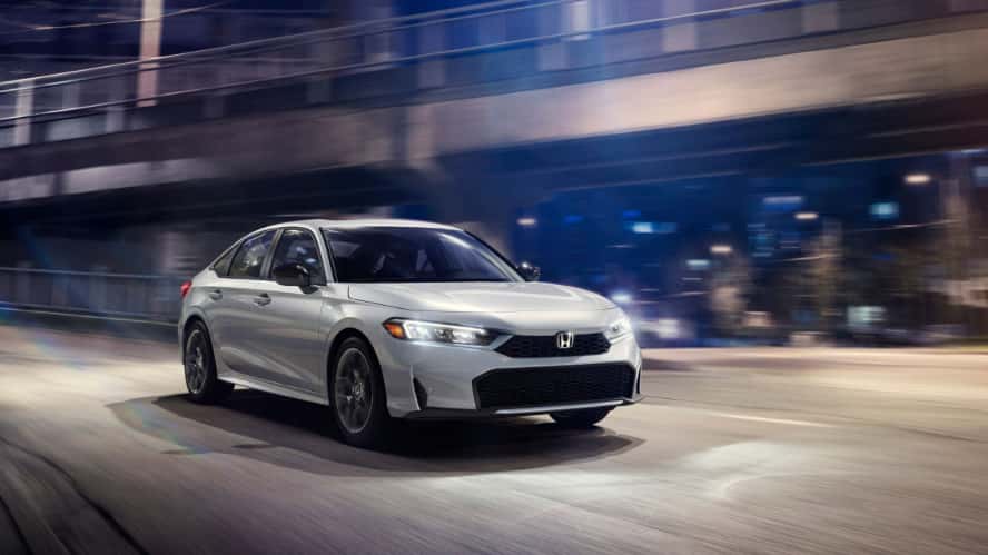 A white Honda Civic Hybrid driving around a city on the highway at night.