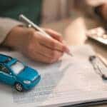 A person signing a lease agreement with a blue, toy car on top of the paperwork.