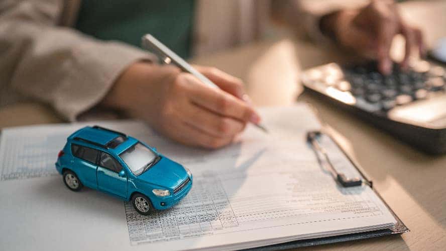A person signing a lease agreement with a blue, toy car on top of the paperwork.