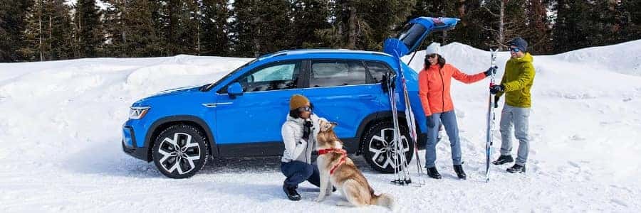 a 2023 blue taos parked in the snow with skiers gathered around it