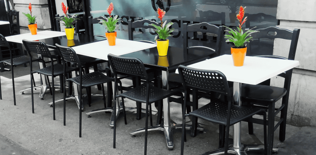 Tables and Chairs on an Outdoor Patio with Yellow and Orange Vases with Red Flowers Waiting for Diners