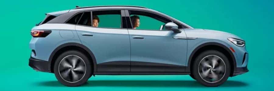 a light blue volkswagen SUV in front of a teal background. A family smiles inside