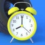 a yellow analog alarm clock in front of a pile of tires