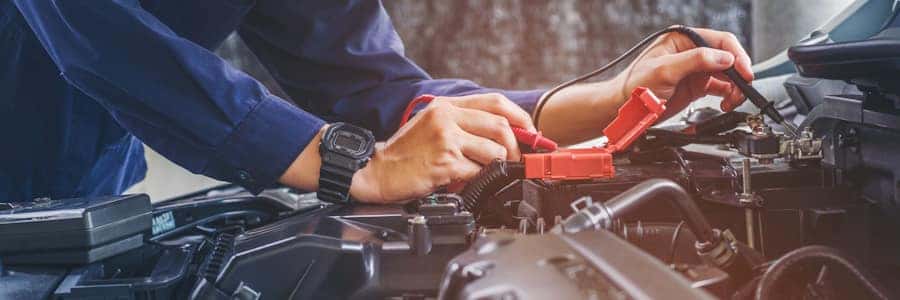 person testing a car battery with the hood up person testing a car battery with the hood up