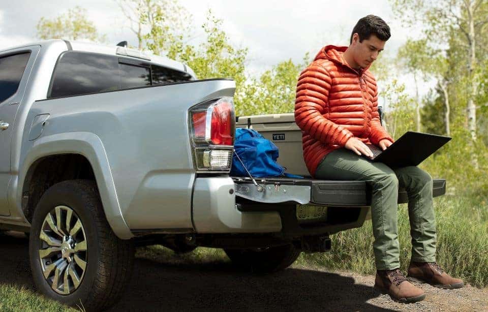 a 2020 Toyota Tacoma parked outdoors with a man sitting on the tailgate using a laptop. 