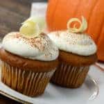Two pumpkin cupcakes on a plate next to a pumpkin in the background